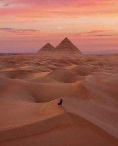 two pyramids in the desert at sunset with a lone person standing on one side