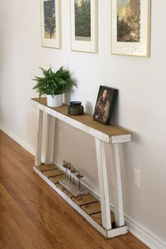 a wooden table with two pictures on the wall and a potted plant next to it