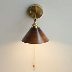 a wall light with a wooden shade hanging from it's side on a white wall