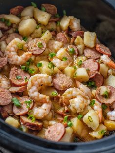 a crock pot filled with sausage, potatoes and shrimp next to green onion garnish