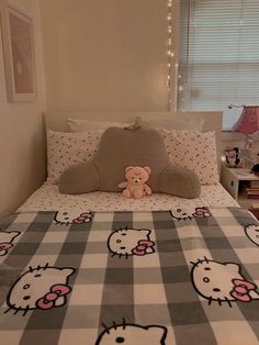 a teddy bear sitting on top of a bed with hello kitty bedspread and pillows