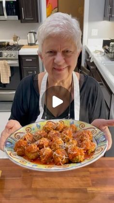 an older woman holding a plate with meatballs on it in her hands and pointing to the camera