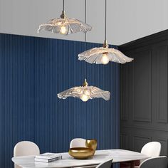 three lights hanging from the ceiling above a dining room table with white chairs and a blue wall