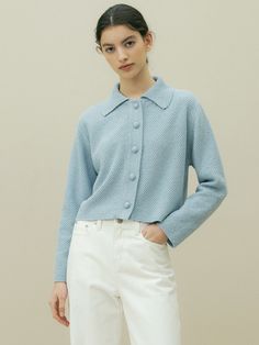 a woman wearing a light blue sweater and white pants with her hands on her hips