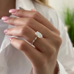 a woman's hand with a diamond ring on her left hand, wearing a white shirt