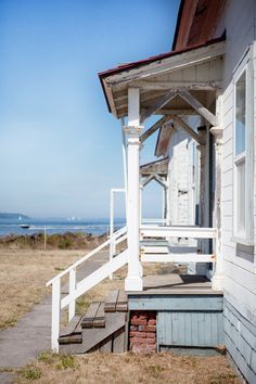 an old white house sitting on top of a grass covered field next to the ocean