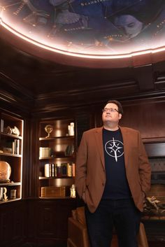 a man standing in front of a book shelf with books on it and a painted ceiling