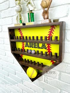 a wooden shelf with baseballs and trophies on it's sides, hanging from a brick wall