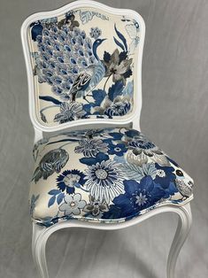 a blue and white chair with a floral pattern on it's back, sitting in front of a gray background