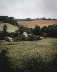 an old farm house sitting in the middle of a lush green field next to trees