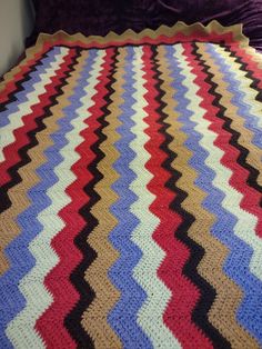 a crocheted blanket on a bed with purple and red pillows in the background