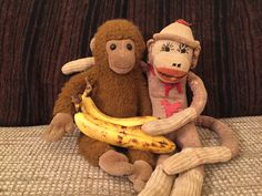 two stuffed monkeys sitting next to each other on a couch with bananas in front of them