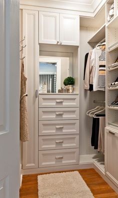 a white closet with lots of drawers and clothes hanging on the shelves, along with a rug