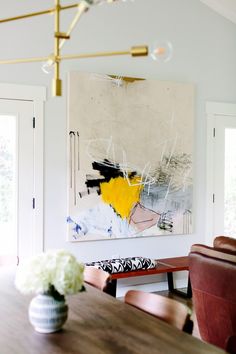 a dining room table with chairs and a large painting on the wall behind it,