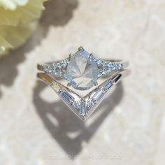 a white diamond ring sitting on top of a table next to a yellow and white flower