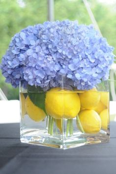 a clear vase filled with lemons and blue hydrangeas on top of a table