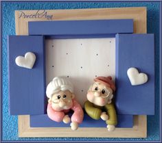 two small figurines are sitting in a blue frame with hearts on the wall