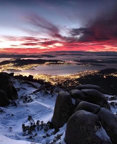 the sun is setting over a mountain with snow on it and lights in the distance