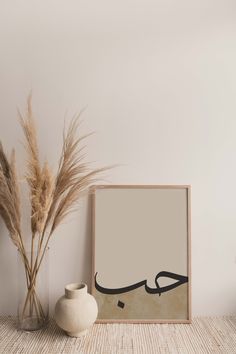 there is a vase with some dry grass in it next to a framed photograph on the wall