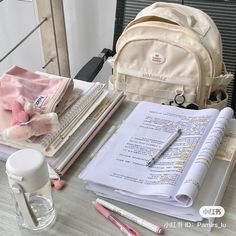 a backpack, notebooks and pens are on a table next to an open book