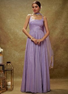 Embrace timeless elegance with the Lavender and Gold Sequin Embroidered Anarkali Gown, expertly crafted from luxurious viscose georgette. This lavender gown is adorned with intricate sequin and threadwork embroidery, bringing a touch of opulence to its design. The flattering strappy round neckline and chic back cutout at the waist introduce a modern flair to the traditional silhouette. Its flowy, floor-length design exudes regal charm, perfectly complemented by the matching net dupatta with delicately embroidered scallop lace. Ideal for Mehndi, Sangeet, or as wedding guest attire, this ensemble seamlessly blends classic allure with contemporary sophistication Composition : Anarkali - Viscose Georgette and Dupatta - Soft net Care: Dry Clean Only and Vacuum Storage This product can be custom Sequin Georgette Anarkali Set For Reception, Georgette Anarkali Set With Sequins For Receptions, Eid Georgette Sequin Gown, Elegant Georgette Anarkali Set With Sequins, Festive Georgette Gown With Sequins, Floor-length Georgette Gown With Intricate Embroidery, Elegant Floor-length Anarkali Set With Sequins, Eid Maxi Gown With Sequins, Festive Sequined Georgette Gown