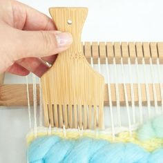 someone is weaving yarn on a loom with a small wooden comb in the foreground