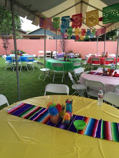 tables and chairs are set up under the tent for an outdoor party with colorful decorations