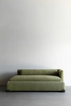 a green couch sitting on top of a cement floor next to a white painted wall