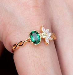 a close up of a person's hand wearing a ring with an emerald and white flower