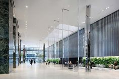 an empty lobby with people sitting at tables and plants on the wall behind glass partitions