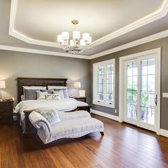 a large bedroom with hardwood floors and white bedding, chandelier, windows, and wooden flooring