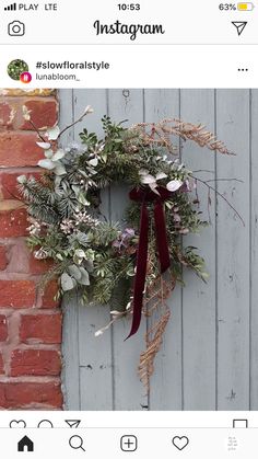 a wreath is hanging on the side of a door with greenery and red ribbon