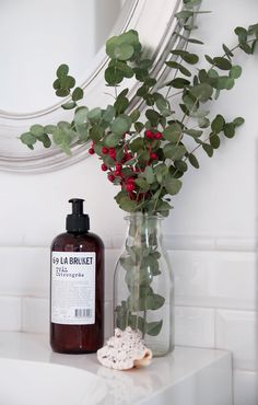 a vase filled with red flowers next to a bottle of lotion on a counter