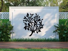 a large metal tree on the side of a white wall in front of some bushes