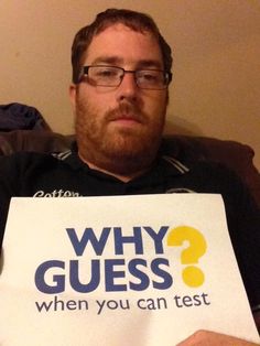 a man sitting on a couch holding a sign that says why guess? when you can test