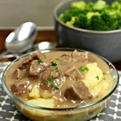 a glass bowl filled with beef and gravy on top of a checkered table cloth