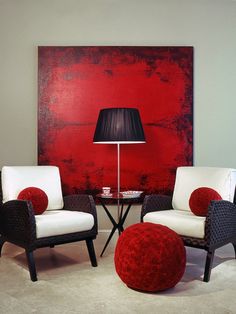 two chairs and a table in front of a red wall with a lamp on it