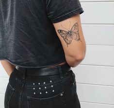 a woman with a butterfly tattoo on her back, standing in front of a white brick wall