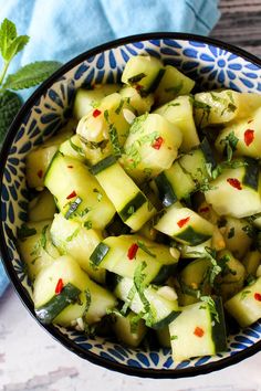 a bowl filled with cucumber and herbs on top of a wooden table next to a blue towel