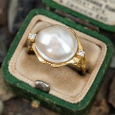 This pretty mabé pearl ring is crafted of 18k yellow ring and features a centered mabé pearl with a diamond accent on each sides. The ring is currently a size 6.25. The pearl is lightly blemished and one of the diamond accents has an unnoticeable chip. Luxury Antique Style Pearl Ring With Cabochon, Luxury Oval Diamond Pearl Ring, Luxury Modern Pearl Engagement Ring, Luxury Timeless Pearl Ring, Luxury Classic Pearl Ring With Single Cut Diamonds, Luxury Oval Heirloom Pearl Ring, Luxury Victorian Oval Pearl Ring, Luxury White Heirloom Pearl Ring, Luxury Pearl Ring With Gemstone