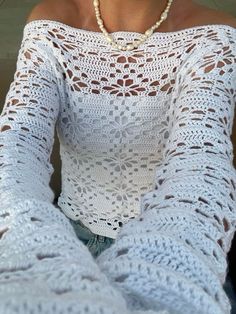 a woman wearing a white crochet top and pearls is posing for the camera