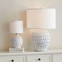 two white vases sitting on top of a dresser next to a lamp with a white shade