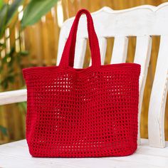 a red crocheted tote bag sitting on top of a white bench next to a potted plant