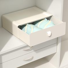 an open drawer with pillows in it on top of a white table and drawers below