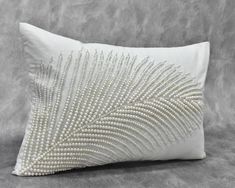 a white pillow with beading and pearls on the front, sitting on a gray background