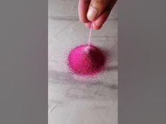 a hand is sprinkling pink powder onto the ground with a toothpick