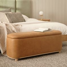 a bedroom with a bed, nightstand and footstool on carpeted flooring