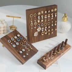 three wooden boxes with earrings on them sitting on top of a white table next to other items