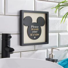 a bathroom sink with a mickey mouse sign above it and a plant in the corner