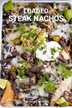 loaded steak nachos in a casserole dish with sour cream and avocado